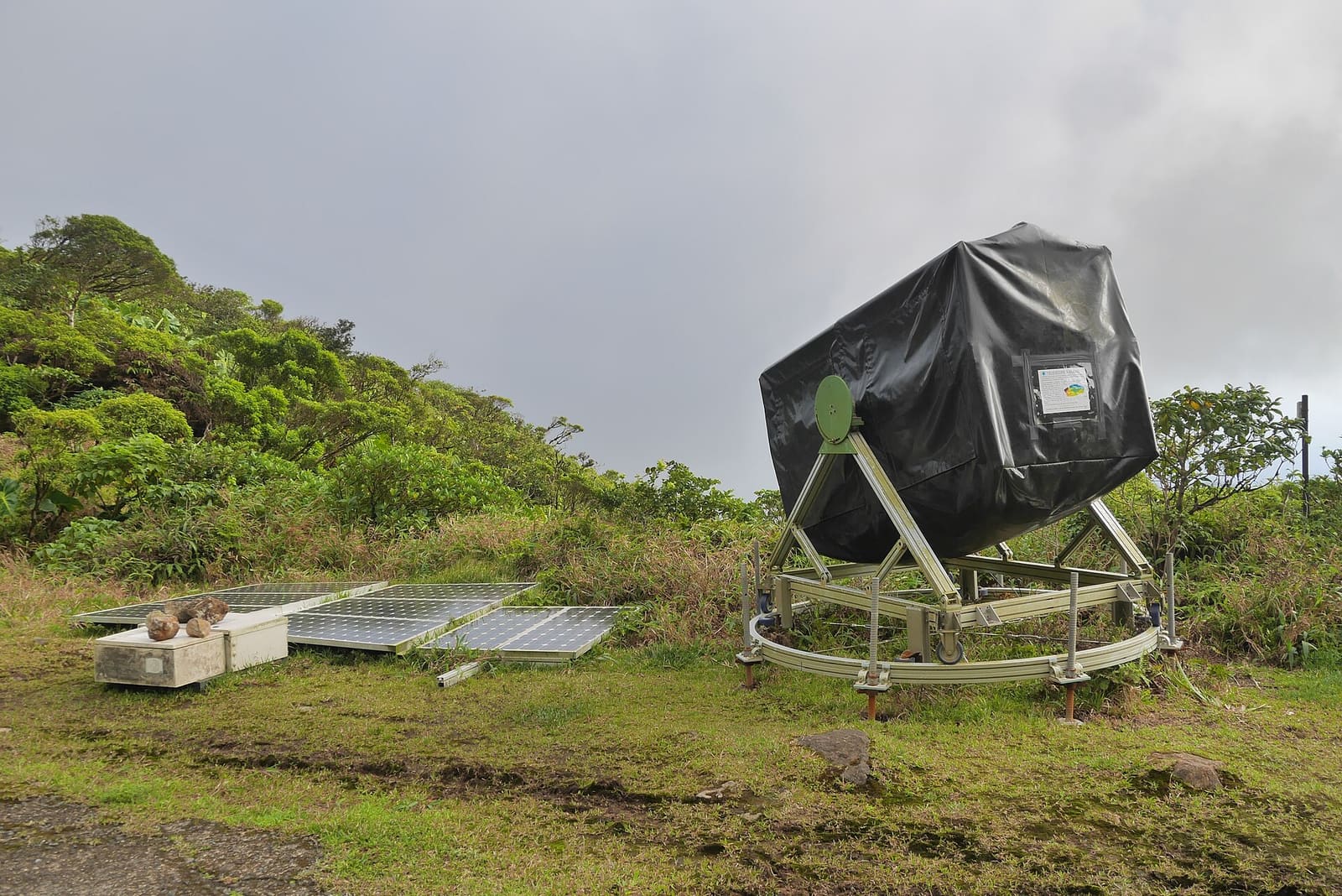 A muon telescope under a black cover on a green hillside of La Soufrière volcano in Guadeloupe