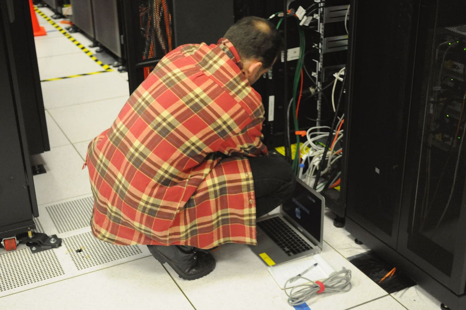 A technician with a laptop working at a server rack in a data center